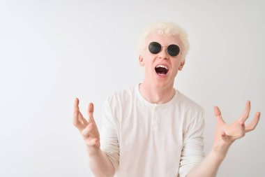 Tişört ve güneş gözlüğü takan genç albino adam beyaz arka planda çılgınca bağırıyor ve agresif bir ifade ve kollarla bağırıyor. Hayal kırıklığı konsepti.
