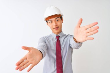 Kravat ve miğfer takan Çinli mimar izole edilmiş beyaz arka planda durup kucaklaşmak için kolları açık gülümseyen kameraya bakıyor. Mutluluğu kucaklayan neşeli bir ifade..