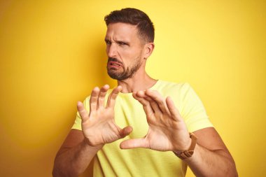 Sarı izole edilmiş arka planda sıradan sarı tişört giyen genç yakışıklı adam tiksindirici ve tiksindirici bir yüz ifadesi takınıyor çünkü tiksinti tepki veriyor. Eller havada. Can sıkıcı bir kavram..