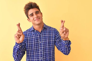 Izole sarı arka plan gesturing parmak üzerinde duran rahat gömlek giyen genç yakışıklı adam umut ve gözleri kapalı gülümseyerek geçti. Şans ve batıl kavram.