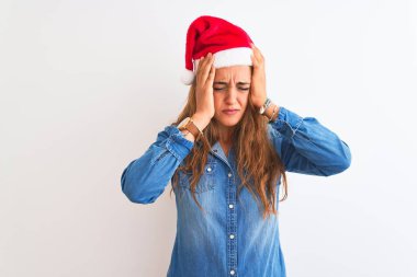 Genç ve güzel kızıl saçlı bir kadın, izole bir arka plan üzerine noel şapkası takıyor. Acı ve migren yüzünden baş ağrısı ve stresten muzdarip. Ellerini başının üstüne koy..