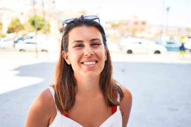Genç ve güzel bir kadın mutlu bir şekilde gülümsüyor güneşli bir yaz gününde şehir sokaklarında yürüyor.