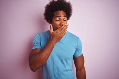 Afro saçlı, mavi tişörtlü, izole edilmiş pembe arka planda duran, esnemekten sıkılmış, ağzı eliyle kapatan Afro-Amerikan bir adam. Huzursuz ve uykulu..