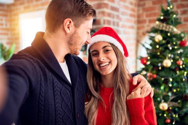 Mutlu ve kendinden emin gülümseyen genç bir çift. Evdeki Noel ağacının etrafında kamerayla selfie çekmek.