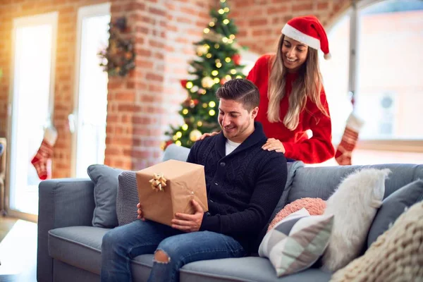年轻漂亮的夫妇面带微笑 既快乐又自信 女人给家里的圣诞树下的男人一个惊喜 — 图库照片