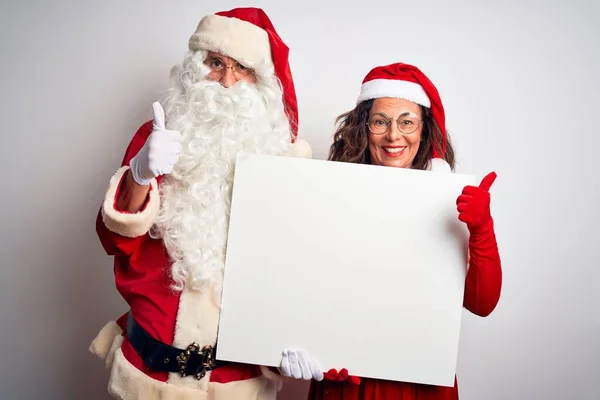 上了年纪的夫妇穿着圣诞老人的服装 举着横幅遮掩在孤独的白色背景上 高兴地看到大大的笑容 做手势 用手指竖起大拇指 很好的标志 — 图库照片