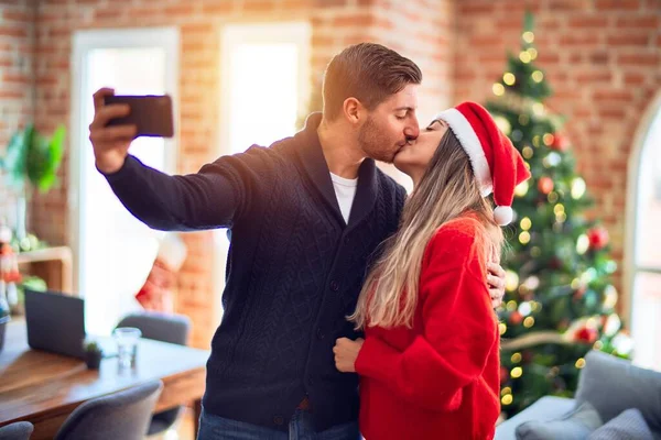 年轻漂亮的夫妇面带微笑 既快乐又自信 在家里 抱着和亲吻通过站在圣诞树旁的相机使自己变得更有魅力 — 图库照片