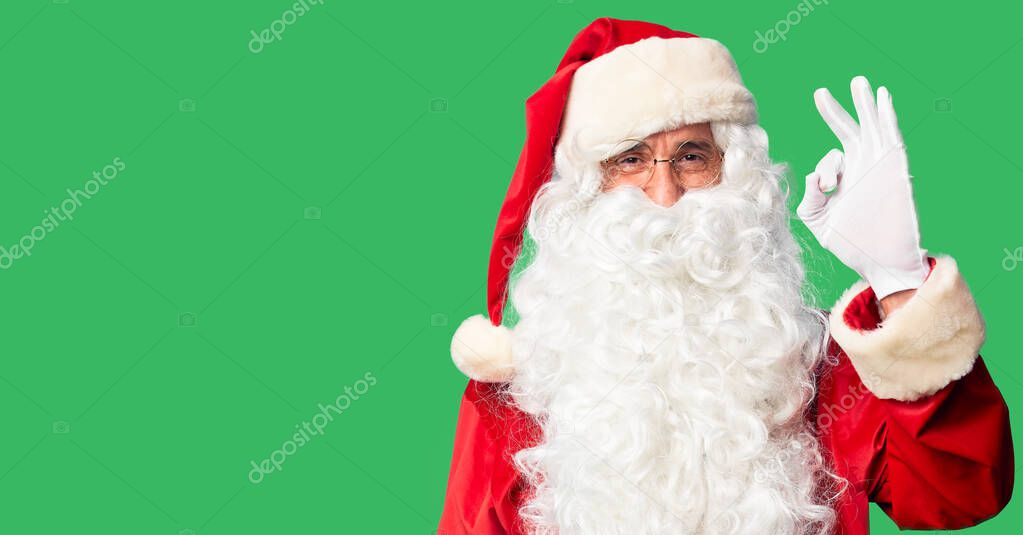 Middle age handsome man wearing Santa Claus costume and beard standing smiling positive doing ok sign with hand and fingers. Successful expression.