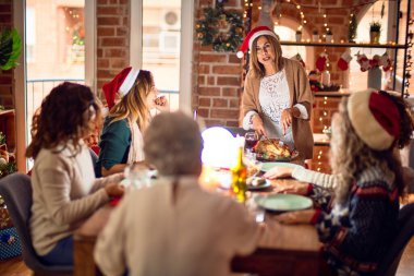 Beautiful group of women smiling happy and confident. Carving roasted turkey celebrating christmas at home clipart