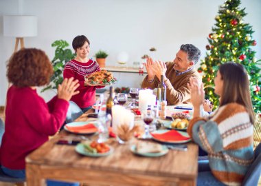 Mutlu ve kendinden emin gülümseyen güzel bir aile. Bir tanesi evde kavrulmuş hindiyi gösteriyor.