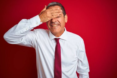 Yakışıklı orta yaşlı işadamı, izole edilmiş kırmızı arka planda duruyor. Gülümsüyor ve elleri yüzünde şaşkınlıktan gözleri kapatıyordu. Kör kavram.