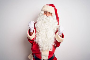 Noel Baba kostümü giymiş orta yaşlı yakışıklı bir adam izole edilmiş beyaz arka planda mutlu ve heyecanlı bir şekilde kollarını kaldırıp, gülümseyerek ve başarı için çığlık atarak kazanan bir jest yapıyor. Kutlama konsepti.