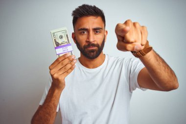 İzole edilmiş beyaz arka planda dolar tutan genç Hintli adam kamerayı işaret ediyor ve sen, el işareti, ön taraftan pozitif ve kendinden emin bir hareket.