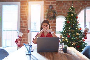 Güzel bir kadın evde dizüstü bilgisayarla oturup Noel ağacı etrafında çalışıyor. Reddedilme ifadesi negatif işaret veriyor.