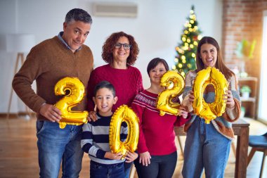Mutlu ve kendinden emin gülümseyen güzel bir aile. Ayakta durup poz vermek 2020 balonu evde Noel ağacı etrafında kutluyor.
