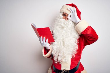 Orta yaşlı bir adam Noel Baba kostümü giyer beyaz arka planda kitap okur. El hareketleriyle gülümser, gözleriyle mutlu yüzle bakar..