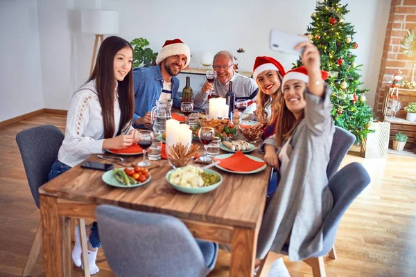 サンタの帽子をかぶっている美しい家族は笑顔で自信を持っています 自宅でクリスマスを祝うスマートフォンで自分で作るロースト七面鳥を食べる — ストック写真