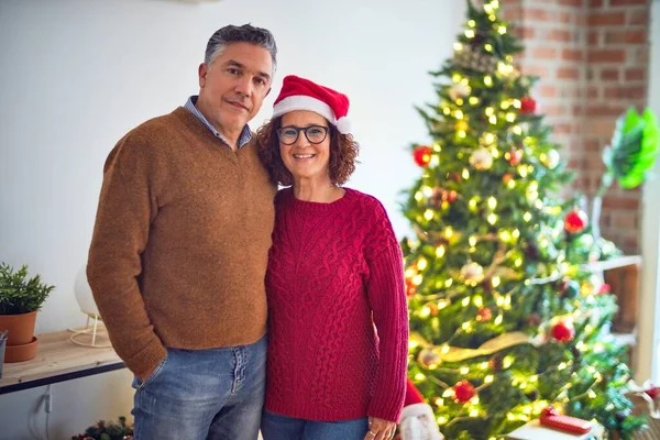 美しい中年のカップル笑顔幸せと自信を持って 家でクリスマスツリーの周りに抱きしめる顔に笑顔で立って — ストック写真