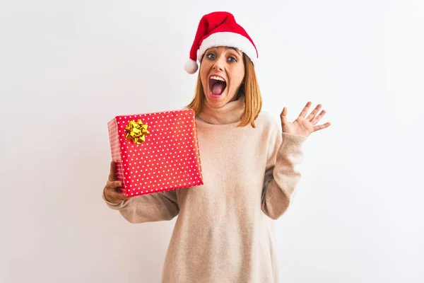 Schöne Rothaarige Frau Mit Weihnachtsmütze Hält Geschenk Vor Isoliertem Hintergrund — Stockfoto