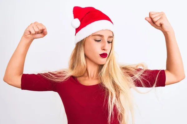 孤立した白い背景にクリスマスのサンタの帽子をかぶっている若い美しい女性は腕の筋肉が誇らしげに笑っていることを示す フィットネスコンセプト — ストック写真