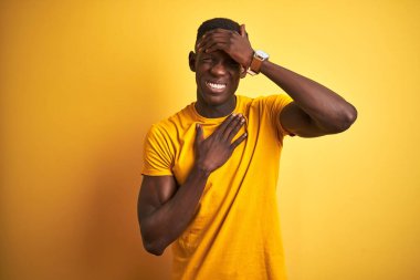 Sıradan tişörtler giyen genç Afrikalı Amerikalı adam izole edilmiş sarı arka planda duruyor. Hastalık ve ateş için alnına dokunuyor. Grip ve soğuk algınlığı için.