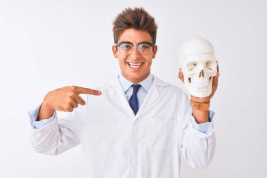 Gözlüklü yakışıklı doktor, izole edilmiş beyaz arka plan üzerinde kafatası tutuyor.