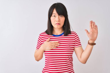 İzole edilmiş beyaz arka plan üzerine kırmızı çizgili tişört giyen genç, güzel Çinli bir kadın. Göğüs ve avuç içleri açık yemin ederek sadakat yemini ediyor.