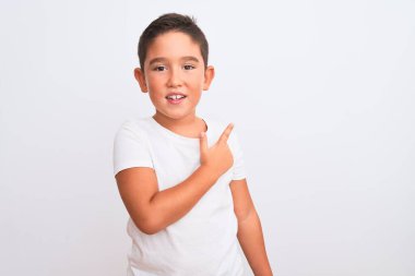 Güzel çocuk, izole edilmiş beyaz arka planda dikilen günlük tişört giyiyor. Yüzünde mutlu ve doğal bir ifadeyle, elleri ve parmaklarıyla yüzünü gösteren bir gülümseme var.