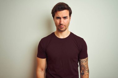 İzole edilmiş beyaz arka plan şüphecisi ve gergin mor tişörtlü, dövmeli genç ve yakışıklı bir adam sorun yüzünden surat asıyor. Negatif kişi.