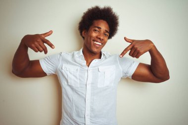 Afro saçlı Afro-Amerikalı bir adam izole edilmiş beyaz arka plan üzerinde duruyor. Yüzünde bir gülümsemeyle, gururlu ve mutlu bir şekilde kendini işaret ediyor..