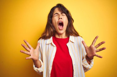 Sarı arka plan üzerinde kırmızı tişört ve çizgili tişört giyen genç ve güzel bir kadın kolları havada ve gözleri kapalı heyecanla haykırarak başarıyı kutluyor. Kazanan konsept