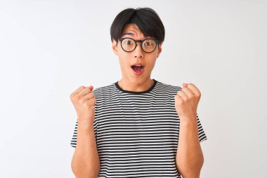 Gözlüklü ve donanma tişörtlü Çinli bir adam izole edilmiş beyaz arka planda durup kollarını kaldırarak ve açık gözlerle başarının şaşkınlığını ve şaşkınlığını kutluyor. Kazanan konsept.