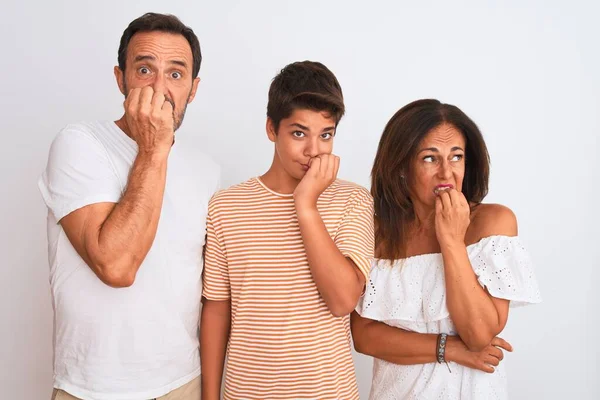 Family of three, mother, father and son standing over white isolated background looking stressed and nervous with hands on mouth biting nails. Anxiety problem.