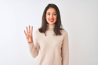 Balıkçı yaka kazak giyen güzel Çinli kadın izole edilmiş beyaz arka plan üzerinde duruyor ve parmaklarını dört numarayı gösterirken kendinden emin ve mutlu bir şekilde gülümsüyor..