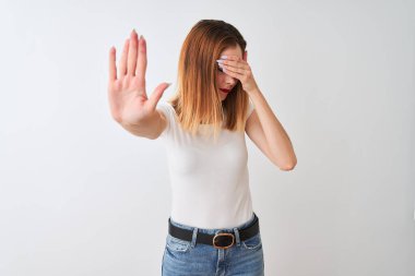 Güzel kızıl saçlı kadın elleri ile gözleri kaplayan izole beyaz arka plan üzerinde duran rahat t-shirt giyen ve üzgün ve korku ifadesi ile stop jest yapıyor. Utanmış ve olumsuz kavram.
