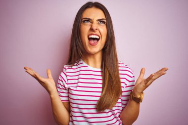 Genç güzel kadın çizgili t-shirt izole pembe arka plan deli ve deli bağırarak ve agresif ifade ve kollar kaldırdı ile bağırarak üzerinde duran giyiyor. Hayal kırıklığı kavramı.