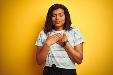 Güzel transseksüel kadın izole edilmiş sarı arka planda tişört giyip elleri göğsünde, gözleri kapalı ve yüzünde minnet dolu bir jest ile gülümsüyor. Sağlık kavramı.