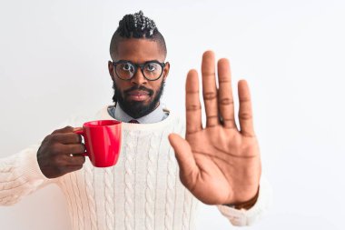 Örgülü Afrikalı Amerikalı bir adam izole edilmiş beyaz arka planda bir fincan kahve içiyor. Açık elle dur işareti yapıyor. Ciddi ve kendinden emin bir ifadeyle.