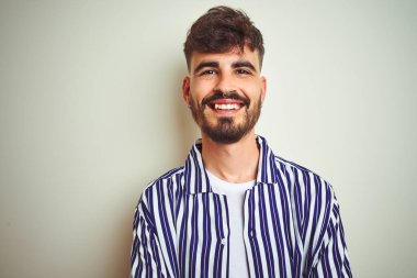 İzole edilmiş beyaz arka plan üzerinde duran çizgili tişörtlü genç adam kollarını kavuşturup kameraya bakarken gülümsüyor. Pozitif kişi.