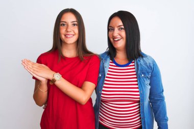 Genç ve güzel kadınlar günlük giysiler giyip izole edilmiş beyaz arka planda ayakta alkışlıyor ve mutlu ve neşeli, gururlu elleri alkışlıyorlar.