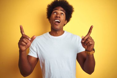 Beyaz tişörtlü, afro saçlı Amerikalı adam izole edilmiş sarı arka planda duruyordu. Şaşırmış ve şaşırmıştı. Parmaklarıyla işaret ediyor ve kollarını kaldırıyordu..