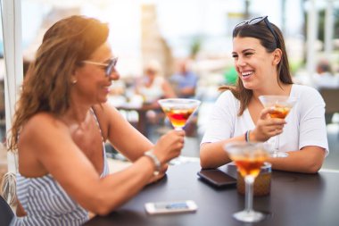 Güzel anne ve kızı restoranın terasında oturmuş kokteyl içiyor ve gülümsüyor.