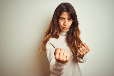 Kışlık süveter giyen genç bir kadın izole edilmiş beyaz arka planda duruyor. Yumruk savunma hareketleriyle dövüşmeye hazır, kızgın ve üzgün yüzlü, sorundan korkan.