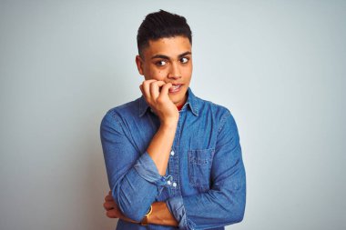 İzole edilmiş beyaz arka plan üzerinde duran kot gömlek giyen genç Brezilyalı adam elleri ağız yiyen tırnaklarla stresli ve gergin görünüyor. Endişe sorunu.