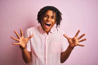 Zarif gömlekli Afro-Amerikan bir adam izole edilmiş pembe arka planda dikilip çılgın ve hayret verici başarısını kutlarken kollarını kaldırmış ve gözleri açık bir şekilde heyecanla haykırıyordu. Kazanan konsept