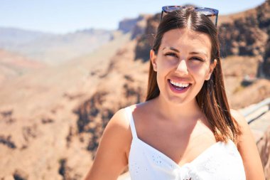 Genç ve güzel bir turist kadın dağ manzarasında mutlu bir şekilde gülümsüyor yaz tatilinin tadını çıkarıyor.