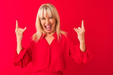 Soyutlanmış kırmızı arka planda duran zarif tişörtlü, çılgın bir ifadeyle el kaldırarak rock sembolü yapan orta yaşlı kadın. Müzik yıldızı. Ağır konsept.