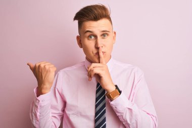 Genç yakışıklı işadamı gömlek ve kravat izole pembe arka plan üzerinde duran dudakları yan el ile işaret parmak ile sessiz olmak isteyen giyiyor. Sessizlik ve gizli kavram.