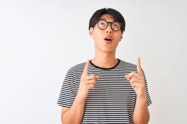 Gözlüklü ve donanma tişörtlü Çinli bir adam izole edilmiş beyaz arka planda duruyor. Şaşırmış ve şaşırmış bir şekilde yukarı bakıyor ve parmaklarıyla işaret ediyor ve kollarını kaldırıyor..