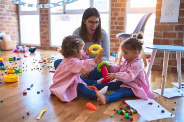 Young beautiful teacher and toddlers wearing uniform building pyramid using hoops at kindergarten clipart